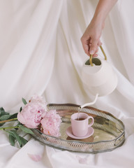 Peonies on a tray with a cup and a teapot white fabric background