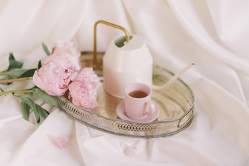 Peonies on a tray with a cup and a teapot white fabric background