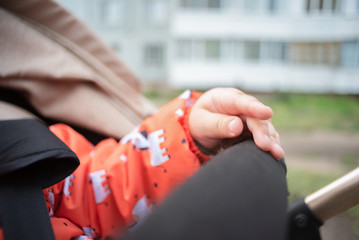 Child hand is holding a handle of baby carriage.