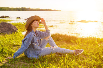 woman in hat and jeans sits on the background of the sea