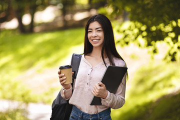 Smiling Asian Student Girl With Backpack And Laptop Enjoying Takeaway Coffee Outdoors