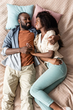 top view of young african american couple in casual clothes lying in bed and looking at each other