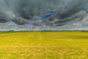 Arid desiccating meadow landscape with footpath Smitskade between the villages of Lageraar and Ter Aar with a green dike against a sky with dark gray clouds