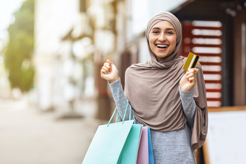 Delighted muslim girl with colorful shopping bags and credit cards