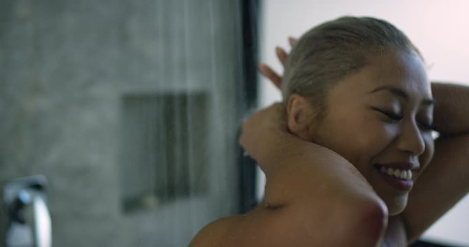 Close up of attractive woman bathing and washing her hair with shampoo first thing in the morning while at home, happy and content ready to go to work and start her day