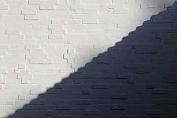 White brick wall is divided into light and shadow parts along the diagonal in form of steps. White and Black. Background. Texture.  Free space for text, quotationor epresentation of opposites.