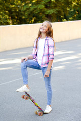 Smiling cute little girl child standing with a skateboard. Preteen with penny board outdoors