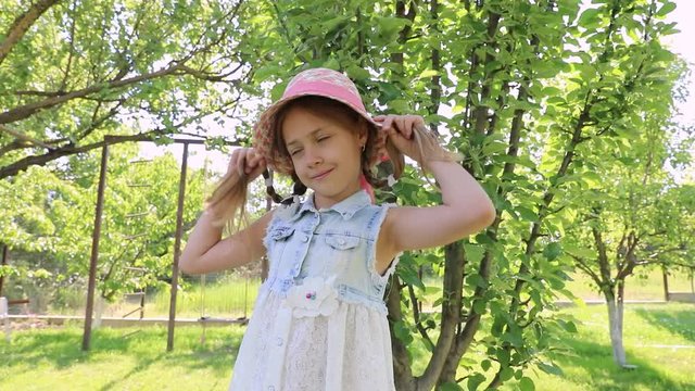Little cute girl dressed in a dress and a hat laughs in a green summer garden. baby laughter, smile. happiness of the child