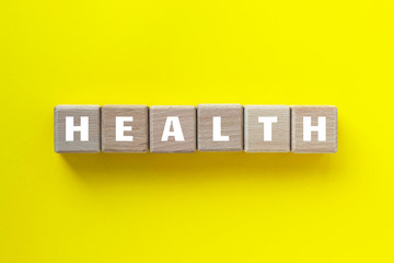 HEALTH word written on wood cubes. Wooden blocks on yellow background. Medical and healthcere concept.