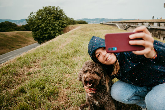 .Young woman in blue raincoat with colorful polka dots enjoying a rainy day in the north of spain with her brown spanish water dog taking photographs