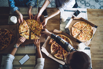 People together grabbing slices of pizza from box at table
