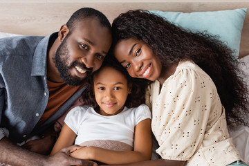 high angle view of african american couple looking at camera near daughter lying in bed