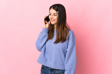Young caucasian woman isolated on pink background keeping a conversation with the mobile phone