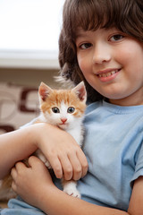 Boy playing with baby cat. Child and kitten at home.