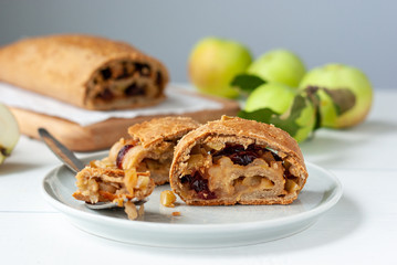 Homemade apple strudel with fresh apples and cranberries on a white wooden table.