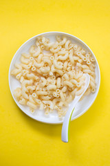 boiled pasta on child plate with spoon on yellow background