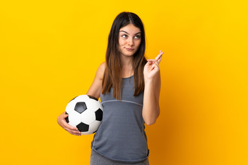 Young football player woman isolated on yellow background with fingers crossing and wishing the best