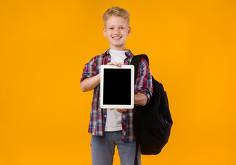 Smiling school boy showing tablet screen at camera