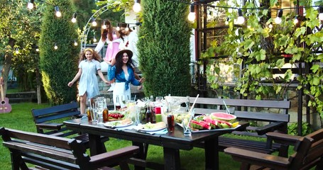 Happy multi-ethnic young people gathering together in garden. Caucasian handsome boys and beautiful girls having party outdoor. Asian cheerful girl smiling and hugging a friend. Fun concept