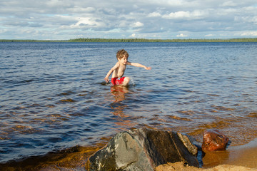 Boy hurries out of the cold water of Kanozero lake. Kola Peninsula, Murmansk Oblast, Russia.