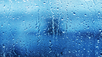 Drops of heavy rainfall on the clear transparent glass of the window in cloudy weather during the day. Sadness and melancholy. Dampness. Bad weather.
