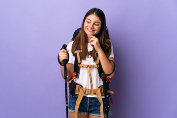 Young woman with backpack and trekking poles isolated on purple background looking to the side and smiling