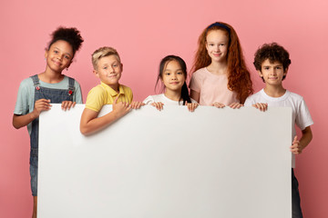 Cute diverse schoolchildren with blank banner over pink background, mockup for your design