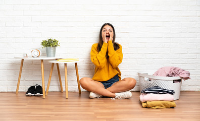 Young woman sitting on the floor at indoors with clothes basket shouting and announcing something