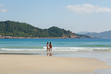 two girls in bekin with a white surfboard are standing near the sea, summer, heat, sunny day, clear sea water, wave