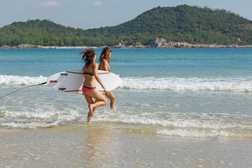 two girls in bekin with a white surfboard enter the blue sea, summer, heat, sunny day, clear sea water, wave