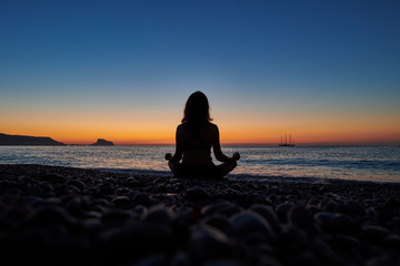 Fototapeta premium Yoga and meditation on calm beach at sunrise, Young fit women, Woman doing yoga outdoors at sunrise on the beach - Woman meditating at morning time - Fitness exercise concept for healthy lifestyle