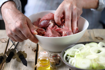 Selective focus. Chef's hands are preparing meat kebab with onions. A bowl of raw meat and a bowl of onions. Barbecue cooking.