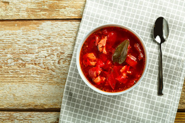 A plate of borscht with chicken on a napkin with a spoon on a wooden table.