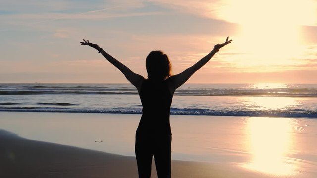 Silhouette of Happy slim woman with arms raised up on the beach at sunset