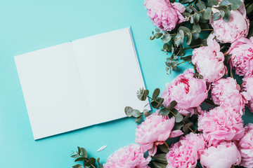 Feminine workspace with notebook, pink peony, eucalyptus flower on blue background. Top view, copy space. Blogger, feminine business concept. Flat lay. Birthday, Woman day. Mock up