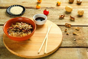 Obraz na płótnie Canvas Funchoza with vegetables and mushrooms in a clay plate on a round stand next to chopsticks and soy sauce. Vegetables and sesame seeds next to them.