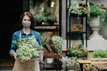 Opening store during COVID-19 epidemic. Woman in protective mask takes out box of plants