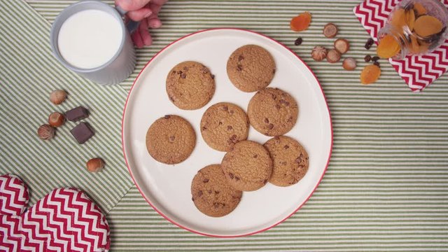 Top view hands take fresh cookies from plate and mugs with milk. Woman's and men's hands take fresh home cookies 