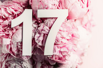 Creative layout. Peony flowers, digit seventeen. Birthday greeting card with inscription 17. Anniversary concept. Top view. Copy space. Stylish white numeral on flower background. Numerical digit