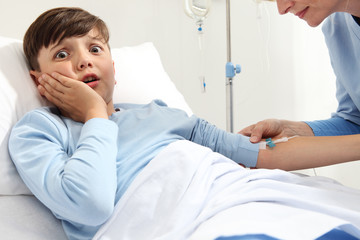 Child lying in bed in hospital room scared by the needle of the drip and nurse medicating him