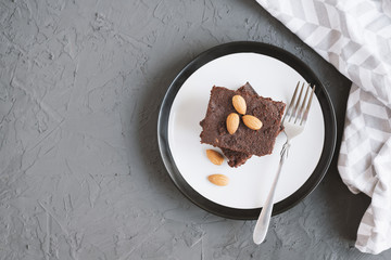 Homemade chocolate brownie with almond nuts served on a plate with fork and napkin, top view
