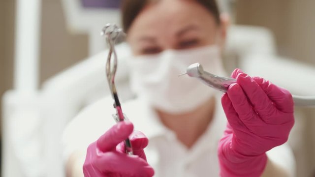 A closeup of a woman dentist holding two drills. She is in disposable gloves.