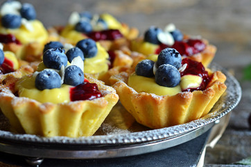 Tartlets with pudding, blueberries and jam on a rustic tray