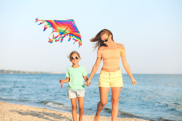 Woman and her little daughter flying kite on sea beach at resort