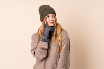 Teenager Ukrainian girl with winter hat isolated on beige background thinking an idea