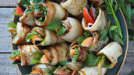 Vegetable rolls with spicy grass on a wooden background.A dish of tomatoes wrapped in fried eggplant wedges.