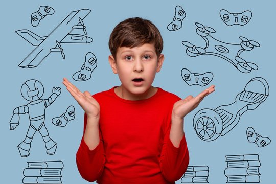 Studio shot of a serious boy  wondering something spreading his arms to the side, isolated on blue with dudles
