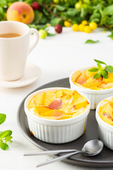 Delicious clafoutis made from white yogurt and peaches, cherry plum and peach dessert in portioned bowls on the table with a cup of juice