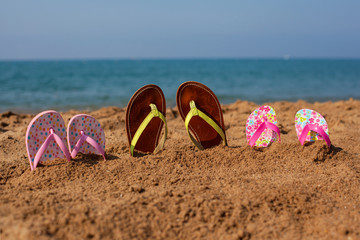 Three pairs of slippers for adults and children on the beach by the sea.