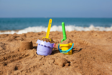 Children's buckets and shovels with sand on the beach against the background of the sea wave.